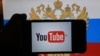 RUSSIA -- A hand holding a smartphone with the logo of the Youtube video sharing website on the screen, in front of a computer screen showing a Russian national flag and coat of arms, St. Petersburg, December 2, 2016